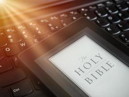 close-up do leitor de e-book com a Bíblia Sagrada em um teclado de laptop com o conceito de luz de raios de sol foto