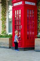 uma pequeno Garoto quer para entrar uma vermelho telefone cabine. foto