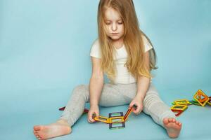 pequeno menina jogando com colorida magnético construtor brinquedo em azul fundo foto