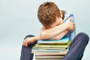 estudante chateado sentado com uma pilha de livros escolares e cobre o rosto com as mãos. menino dormindo em uma pilha de livros didáticos foto