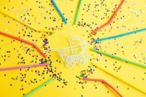 festa de aniversário carrinho de bebê com lantejoulas de confete de estrelas e canudos multicoloridos em fundo amarelo foto