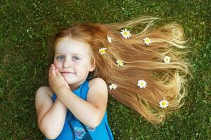 retrato de uma linda garotinha com cabelo vermelho saudável com flores de camomila deitada na grama foto