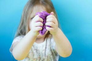 loira esticando o lodo roxo isolado no fundo azul. criança brincando com brinquedo de lodo. fazendo lodo. copie o espaço. foto