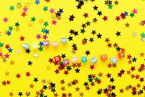 feliz aniversário de inscrição e confetes multicoloridos em forma de estrelas em fundo amarelo foto