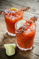 dois copos de bloody mary com fatias de bacon foto