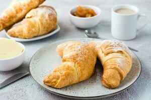 uma par do fresco crocantes croissants em uma placa, uma copo do café e taças do geléia e manteiga em uma luz texturizado fundo. café pausa ou café da manhã foto