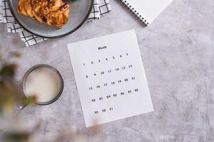 calendário Folha para planejamento durante uma lanche com café com leite e pães dentro fika Tempo topo Visão foto