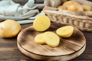 fresco amarelo batatas cortar para dentro peças em uma borda e uma cesta com tubérculos em uma de madeira mesa. vegetariano Comida. foto