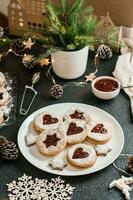 pronto Linzer biscoitos com baga geléia em uma prato e Natal decorações em uma Sombrio fundo. cozinhando Natal guloseimas. estilo de vida. vertical Visão foto