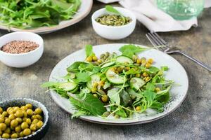 fresco verde salada com pepino, ervilhas e Rúcula, mizuna e acelga folhas em uma prato em a mesa. Vitamina e saudável Comida. vegetariano e flexetariano dieta foto