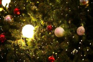 fechar acima decoração bola e luz lâmpada em Natal árvore às noite foto