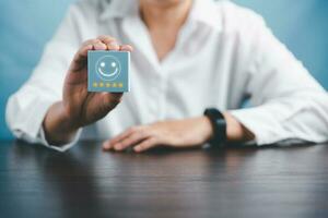 mulher mão segurando feliz face sorrir face ícone em cubo azul objeto. cliente experiência e serviço com satisfação conceito. positivo pensamento, mental saúde avaliação, mundo mental saúde dia. foto