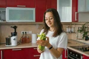 atraente alegre menina é em pé dentro a cozinha com fresco legumes e segurando salsão dentro dela mãos. foto