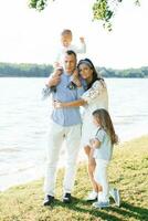 uma feliz família com dois crianças ter Diversão ao ar livre dentro verão de a lago foto