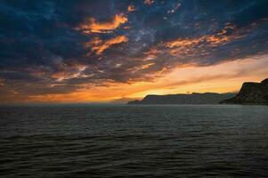 Visão a partir de a mar para a oeste capa dentro Noruega às pôr do sol com Sol raios e pesado nuvens foto