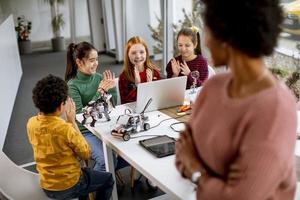 crianças felizes com sua professora de ciências afro-americana com laptop programando brinquedos elétricos e robôs na sala de aula de robótica foto