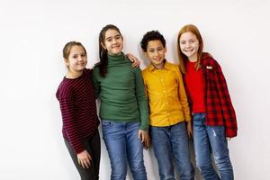 retrato de crianças fofas em jeans olhando para a câmera e sorrindo em pé contra uma parede branca foto