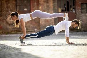 jovem casal fazendo exercícios de flexão para duas pessoas no ambiente urbano