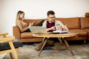 mulher e homem jovem usando laptop para pagamento on-line enquanto estão sentados no sofá em casa