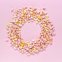 vista de cima dos marshmallows multicoloridos que tem a forma de uma moldura redonda com uma área para texto no centro em um fundo rosa monocromático foto