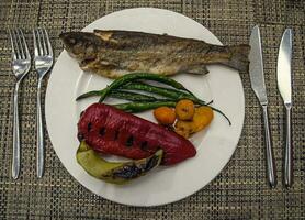 saudável fresco grelhado mar peixe e verde pimentas em uma branco prato foto