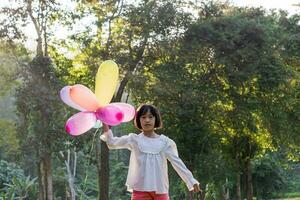 retrato do criança menina jogando com colorida brinquedo balões dentro a parque ao ar livre. foto