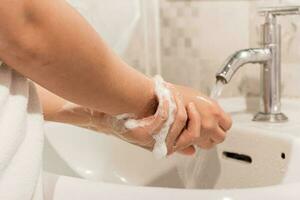 fêmea lavagens dele mãos com Sabonete sobre uma Pia dentro a banheiro. conceito do higiene tratamento. foto
