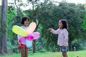 dois criança menina segurando colorida brinquedo balões dentro a parque ao ar livre. foto