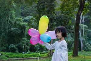 retrato do criança menina segurando colorida brinquedo balões dentro a parque ao ar livre. foto