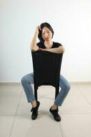 jovem atraente sul leste ásia mulher pose face expressão emoção em branco fundo sentar em cadeira foto