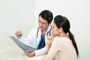 jovem ásia masculino médico vestindo avental uniforme estetoscópio fêmea paciente conversa discutir bochecha foto