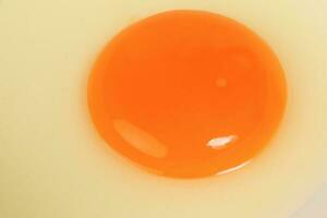 cru ovo gema e branco líquido dentro transparente vidro tigela branco fundo foto