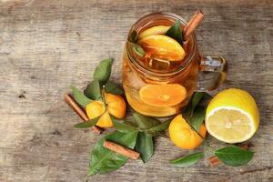líquido gelo limão laranja chá com fatia verde folha canela bastão dentro transparente vidro jarra caneca em rústico madeira fundo todo fruta foto