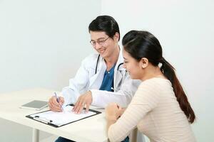 jovem ásia masculino médico vestindo avental uniforme estetoscópio fêmea paciente conversa discutir bochecha foto