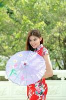 jovem sul leste ásia chinês mulher tradicional traje cheongsam segurando papel guarda-chuva ao ar livre às têmpora foto