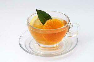 líquido chá limão laranja fatia verde folha canela bastão dentro transparente vidro xícara de chá pires em branco fundo foto