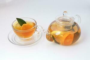 líquido chá limão laranja fatia verde folha canela bastão dentro transparente vidro xícara de chá pires chaleira chaleira em branco fundo foto
