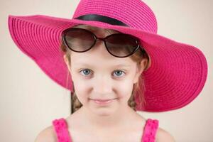 pequeno menina com Rosa vestir chapéu e oculos de sol foto
