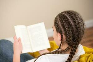 Adolescência menina com tranças lendo livro em amarelo beanbag cadeira foto