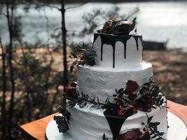 lindo bolo de casamento de creme branco de três camadas com frutas da romã e flores frescas na mesa e velas foto