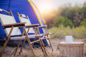 barraca de acampamento com xícara de café na mesa e cadeiras na floresta pela manhã foto