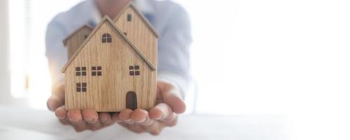 conceito de investimento imobiliário e de propriedade fecha a mão do empresário segurando o modelo de madeira da casa na tampa horizontal foto