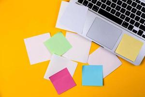 área de trabalho da mesa do escritório em casa com laptop e adesivo de papel no fundo amarelo foto