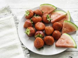 morangos vermelhos maduros e suculentas fatias de melancia em um prato vista de cima foto