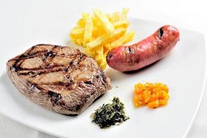 Carnes grelhadas, chouriço e batatas fritas com molho chimichurri foto