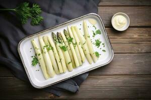 tradicional cozido no vapor branco espargos com Hollandaise molho e ervas Como uma topo Visão dentro a esmalte bandeja em a velho madeira mesa com cópia de espaço em a certo, gerar ai foto