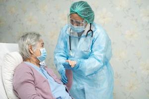 médico asiático usando protetor facial e terno novo normal para verificar paciente proteger segurança infecção covid 19 surto de coronavírus na enfermaria de quarentena do hospital foto