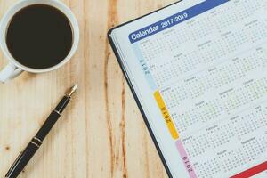 calendário planejador com fonte caneta e quente café em madeira mesa.escritório ferramenta. foto