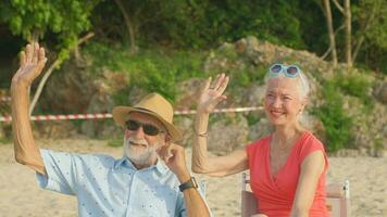 uma casal do idosos sentado dentro cadeiras às a de praia assistindo a Sol e a mar em seus verão período de férias e elas sorrir e apreciar seus período de férias. foto