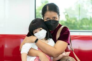 pequeno menina e mãe com cirúrgico mascarar face proteção gripe e vírus surto dentro público transporte. conceito do Novo normal estilo de vida, usando público transporte para viagem para escola foto